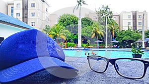 photo of a blue hat and sunglasses with a swimming pool in the background