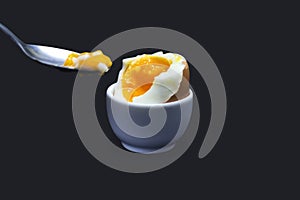 A photo of boiled smash broken hen beige egg and a spoon with yolk isolated on dark blue. Egg`s liquid yolk photo, bright contras