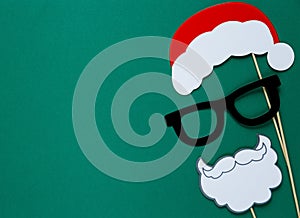 Photo booth colorful props for christmas party - santa hat, glasses, beard on green background.