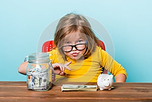 Photo of boss kid. Surprised shocked angry little girl child sitting on chair isolated over blue background holding jar