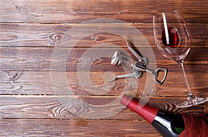 Photo of bottle of wine, corkscrew, wine glass on brown, wooden background.