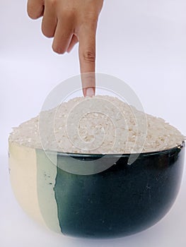 photo of a bowl of rice with a child's index finger, photographed on a white background