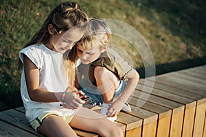 Photo of boy and girl with telephones hands sitting on wooden fence outdoors