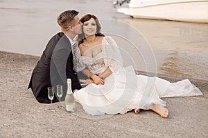 Photo of bride, groom on concrete embankment against backdrop of urban landscape, wide river behind them, they are happy together