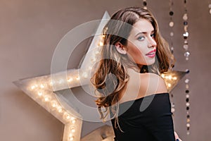 Photo of bright woman with red lips on background of decorative star. Lady in black top coquettishly looks into camera.