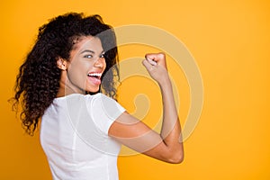 Photo of brunette haired cheerful cute nice curly wavy trendy youngster showing the power in her muscular arm shouting