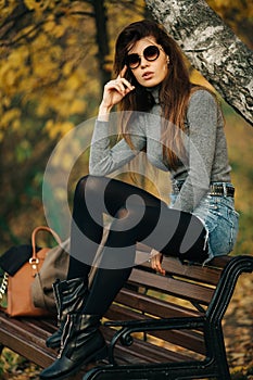 Photo of brunette in sunglasses sitting on bench in autumn park