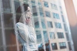 Photo business woman wearing modern suit, talking smartphone and holding papers in hands. Open space loft office. Panoramic window