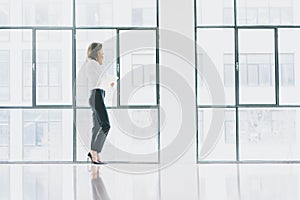 Photo business woman wearing modern suit, talking smartphone and holding papers in hands. Open space loft office