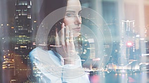 Photo business woman wearing white shirt, talking smartphone. Open space loft office. Panoramic windows, night city background. Wi