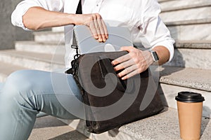 Photo of businessman 30s wearing sunglasses, putting laptop into