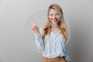 Photo of businesswoman with long curly hair smiling and showing peace sign isolated over gray background