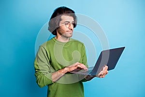 Photo of calm concentrated worker guy hold laptop look screen wear glasses green sweater isolated blue color background