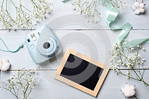 Photo camera and picture frame on blue wooden table. Spring minimal flowers frame, pastel colors, flat lay style, top view. Beauty