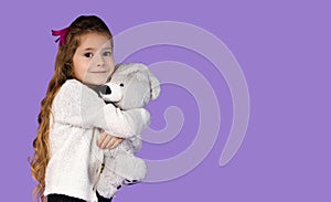 In the photo, it is captured how a little girl plays with her favorite toy, that is, a gray teddy bear, she is very