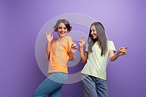 Photo of carefree pretty girls dressed t-shirts dancing having fun smiling isolated purple color background