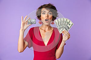 Photo of caucasian brunette woman 20s wearing big straw hat smiling while holding credit card and fan of dollar cash, isolated