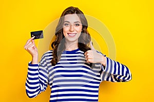 Photo of charming cheerful girl toothy smile hold debit card demonstrate thumb up isolated on yellow color background