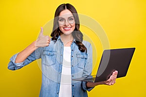 Photo of charming cute lady wear jeans shirt spectacles showing thumb up holding modern device isolated yellow color