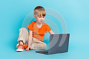 Photo of charming cute little boy sitting floor watching film cartoon online academic classes course isolated on cyan