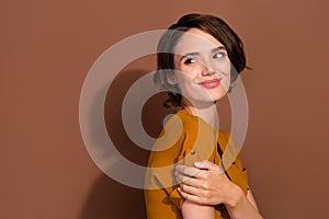 Photo of charming dreamy young woman dressed overall looking back empty space smiling isolated brown color background