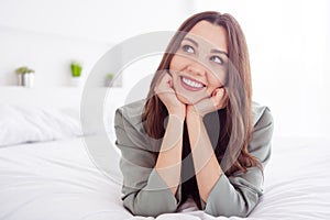 Photo of charming dreamy young woman grey nightwear lying bed arms cheeks smiling inside indoors home room