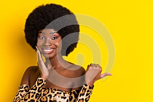 Photo of charming excited dark skin lady wear off-shoulders clothes pointing thumb empty space smiling isolated yellow
