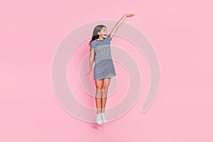 Photo of charming excited girl wear striped dress jumping high measuring empty space isolated pink color background