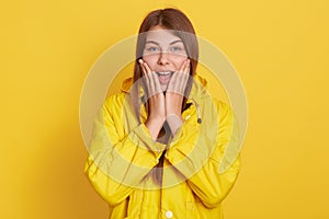 Photo of charming excited young girl with long hair, keeping mouth opened, wear yellow jacket, isolated over color background,