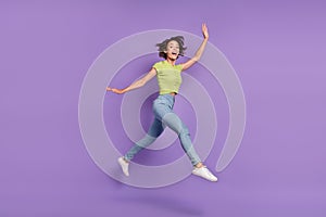 Photo of charming excited young woman dressed green t-shirt jumping walking waving arm empty space isolated purple color