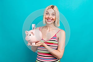 Photo of charming funky young girl holding piggy bank excited demonstrate she save first money salary isolated on cyan