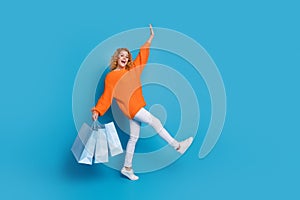 Photo of charming glad woman wear trendy orange clothes carry bags empty space isolated on blue color background