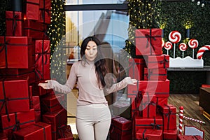 Photo of charming pretty amazed young asian girl standing among many red surprise boxes open mouth excited.