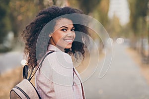 Photo of charming pretty dark skin curly lady walking park after college lectures hold backpack waiting friend join