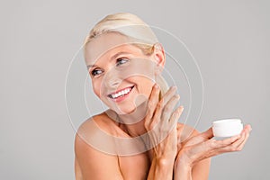 Photo of charming pretty old woman naked shoulders applying face cream  grey color background