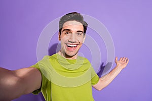 Photo of charming pretty young guy dressed green t-shirt smiling recoding video inviting you empty space isolated purple