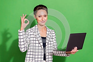 Photo of charming shiny young lady wear plaid outfit spectacles holding modern device showing okey isolated green color