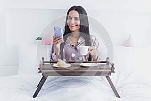 Photo of charming sweet woman nightwear sitting bed enjoying morning coffee reading modern gadget inside indoors home