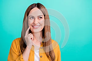 Photo of charming tricky young woman dressed yellow shirt smiling looking empty space finger cheek isolated teal color