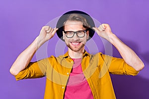 Photo of charming young attractive man hold hands hat smile hipster isolated on purple color background