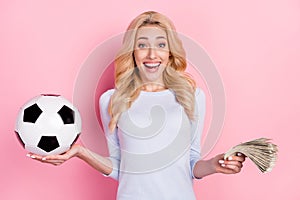 Photo of cheerful amazed young woman hold hands money football bet isolated on pink color background