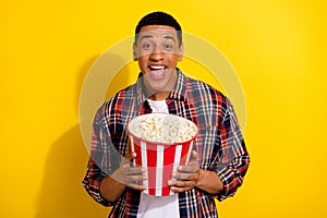 Photo of cheerful attractive glad man wear stylish plaid outfit hold delicious pop corn bucket isolated on yellow color
