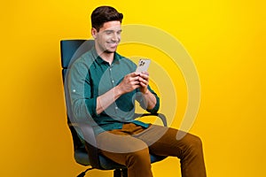 Photo of cheerful attractive man wear trendy clothes sitting armchair writing typing texting sms isolated on yellow