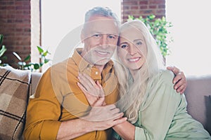 Photo of cheerful attractive old people man and woman sit sofa smile hug free time indoors inside house home