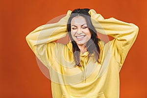 Photo of cheerful beautiful young woman standing isolated over orange background. Showing winner gesture