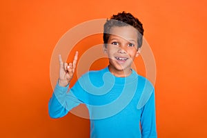 Photo of cheerful boy music lover show arm demonstrate rock freedom symbol dressed blue trendy jumper isolated on orange