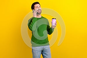 Photo of cheerful candid man wear stylish clothes hand hold cup tasty tea talk phone discuss rumor isolated on yellow