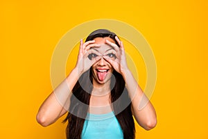 Photo of cheerful childish cute girlish woman sticking tongue out shaping binoculars with her fingers wearing turquoise
