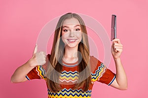 Photo of cheerful cute girl toothy smile hold comb demonstrate thumb up isolated on pink color background