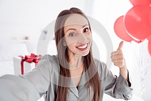 Photo of cheerful cute lady wear grey pajama enjoy getting birthday surprise showing thumb up tacking selfie indoors